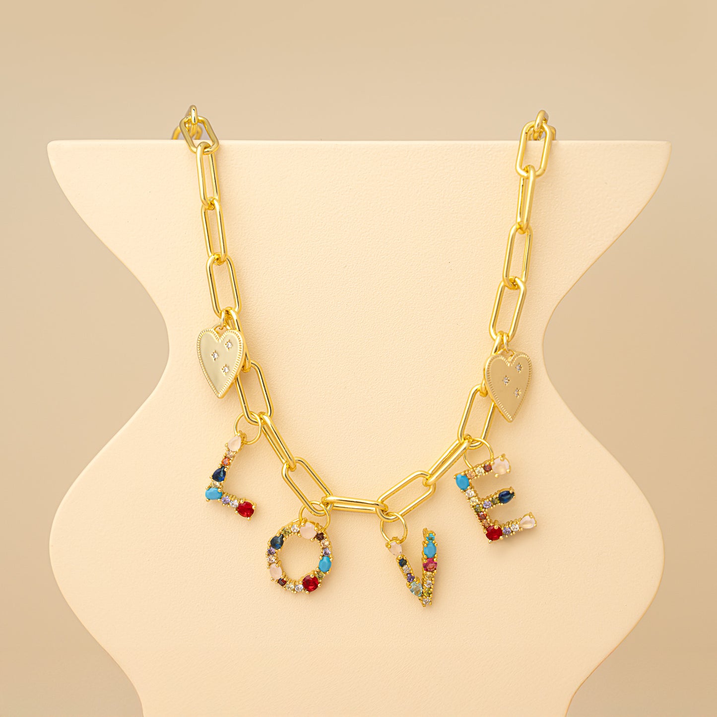 Gold necklace with 'LOVE' charms on a beige stand