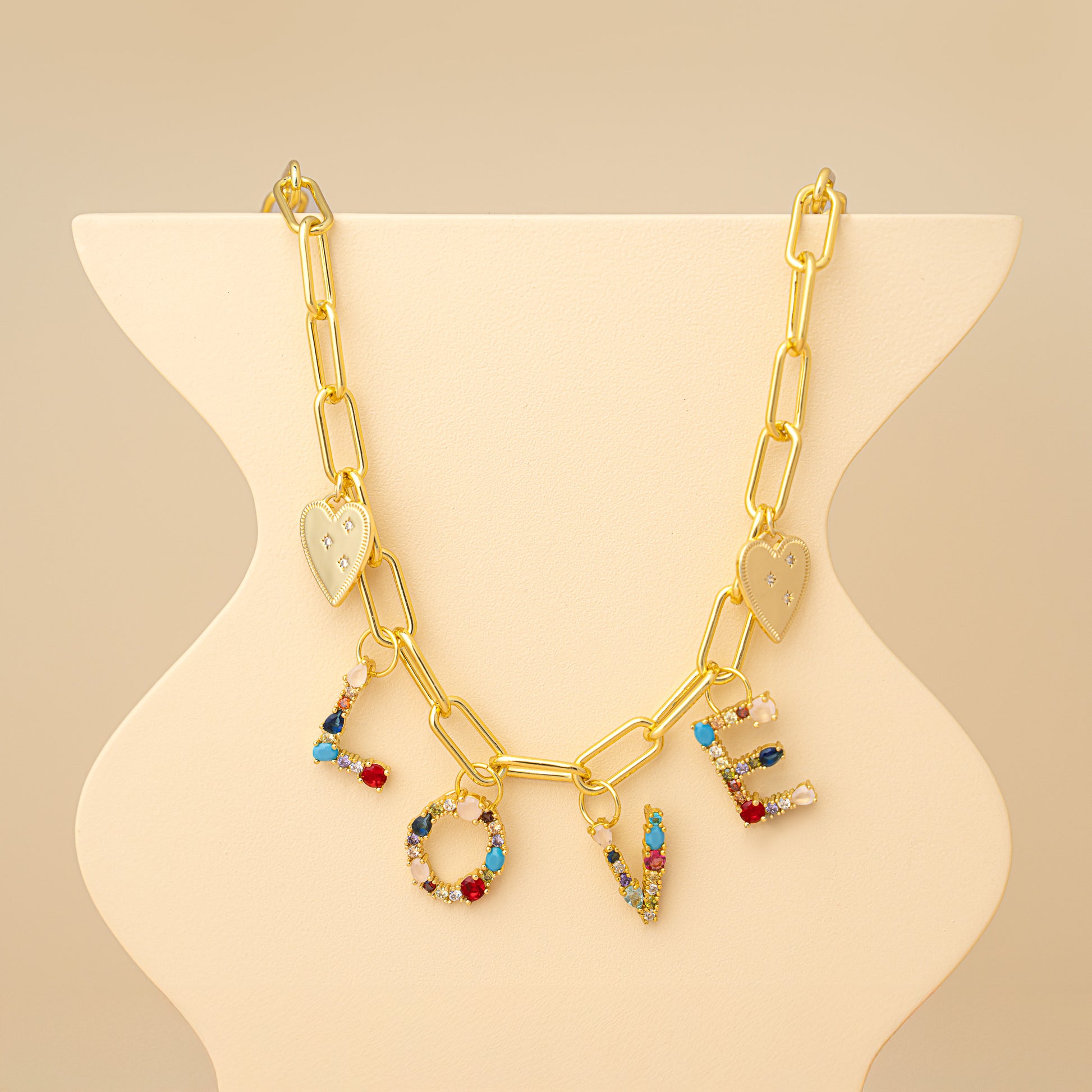 Gold necklace with 'LOVE' charms on a beige stand